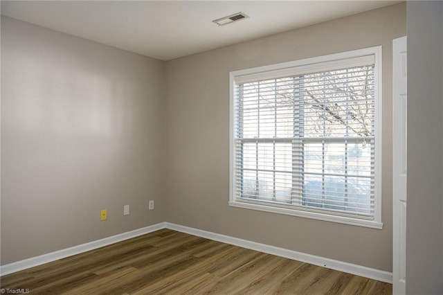 spare room with baseboards, visible vents, and wood finished floors