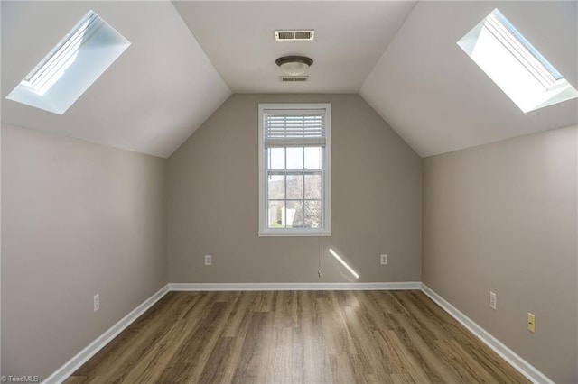 bonus room with lofted ceiling with skylight, visible vents, baseboards, and wood finished floors