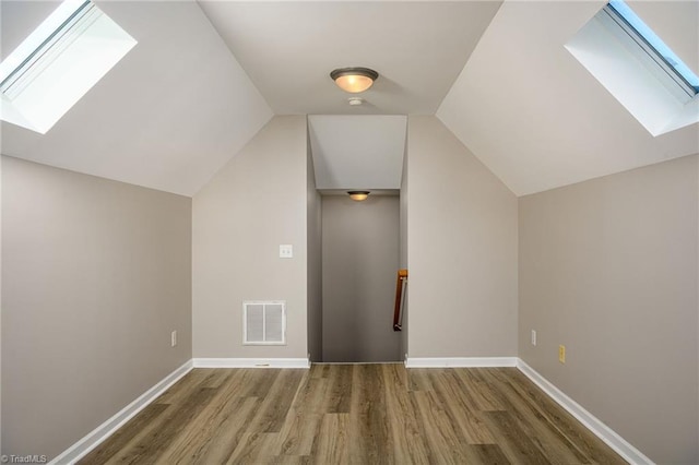 bonus room featuring baseboards, vaulted ceiling with skylight, visible vents, and wood finished floors