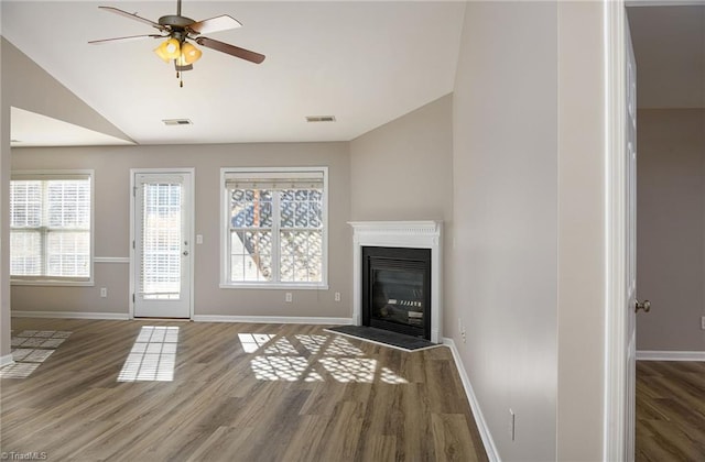 unfurnished living room featuring wood finished floors, visible vents, baseboards, vaulted ceiling, and a glass covered fireplace