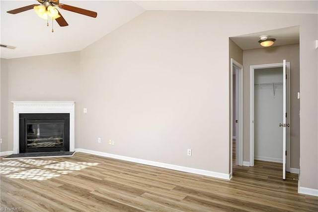 unfurnished living room with wood finished floors, visible vents, baseboards, vaulted ceiling, and a glass covered fireplace