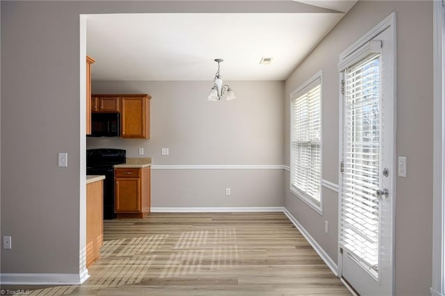 kitchen with brown cabinets, visible vents, an inviting chandelier, light wood-style floors, and black appliances