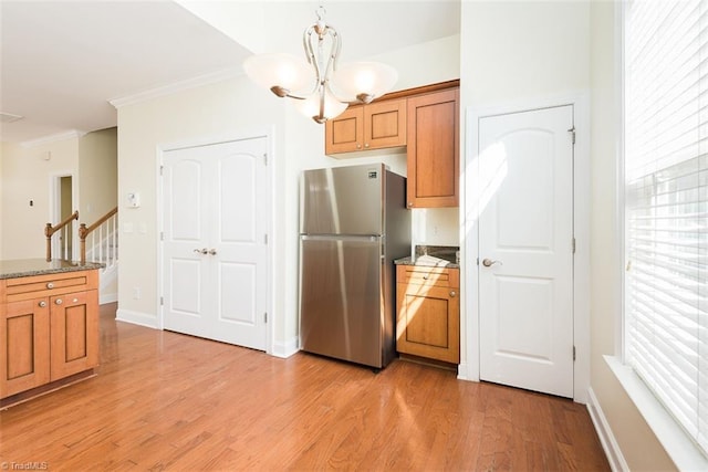 kitchen with stone counters, an inviting chandelier, ornamental molding, freestanding refrigerator, and light wood-style floors