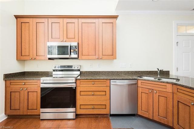 kitchen with appliances with stainless steel finishes, a sink, light wood-style flooring, and ornamental molding