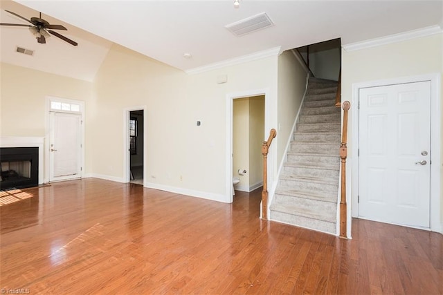 unfurnished living room with light wood-style flooring, a fireplace with flush hearth, visible vents, stairs, and crown molding