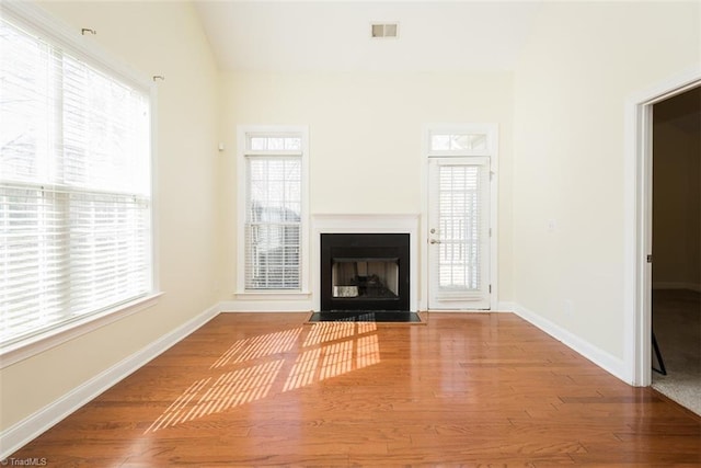 unfurnished living room featuring wood finished floors, a fireplace with flush hearth, visible vents, vaulted ceiling, and baseboards