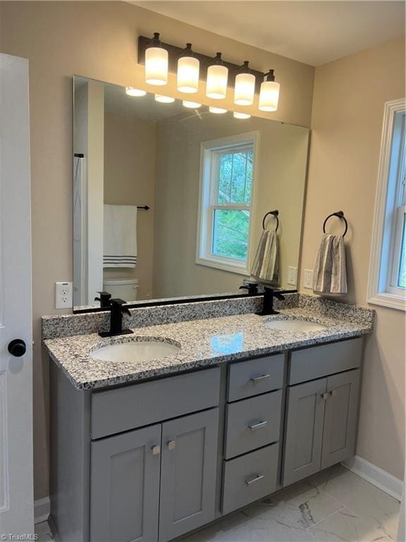 full bath featuring marble finish floor, a sink, baseboards, and double vanity