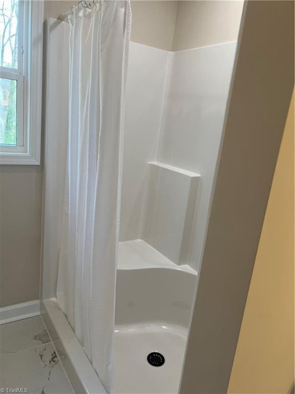 full bath with marble finish floor, a shower stall, and baseboards