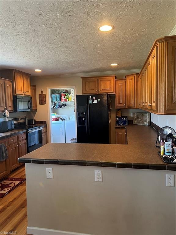 kitchen featuring black appliances, light hardwood / wood-style flooring, separate washer and dryer, a textured ceiling, and kitchen peninsula