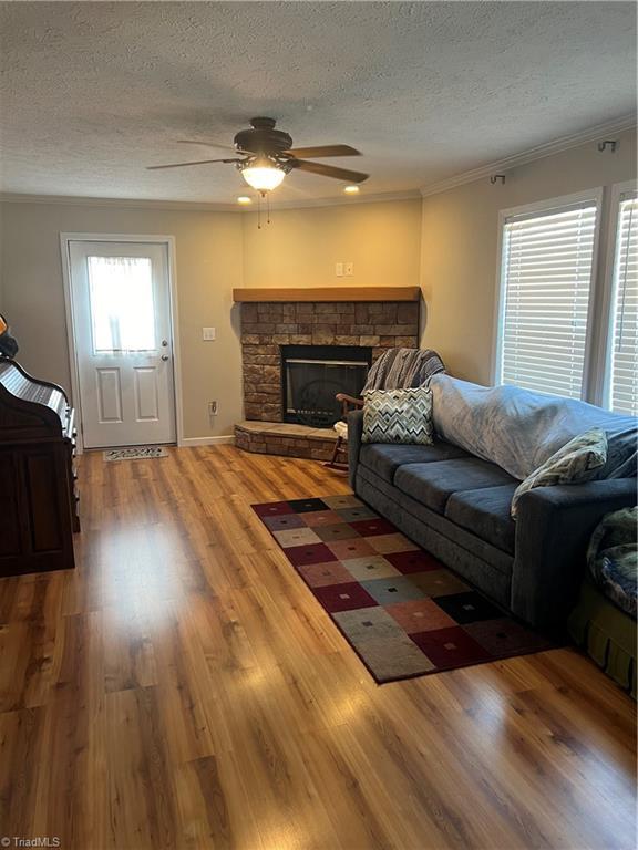 unfurnished living room featuring ceiling fan, a textured ceiling, hardwood / wood-style flooring, a fireplace, and ornamental molding