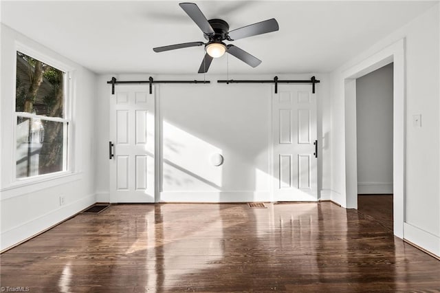 empty room featuring ceiling fan, dark hardwood / wood-style floors, and a barn door