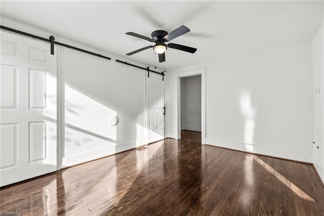 spare room with ceiling fan, dark wood-type flooring, and a barn door