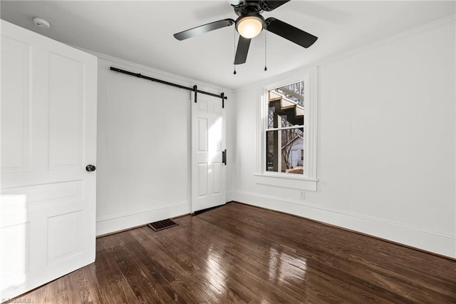 unfurnished bedroom with ceiling fan, ornamental molding, a barn door, and hardwood / wood-style floors