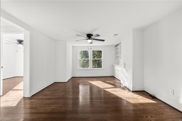 empty room featuring ceiling fan, built in shelves, and dark hardwood / wood-style floors