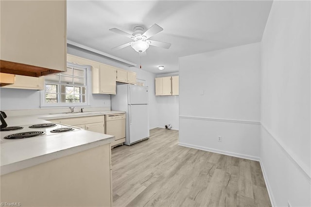 kitchen featuring light wood-type flooring, light countertops, cream cabinetry, white appliances, and a sink