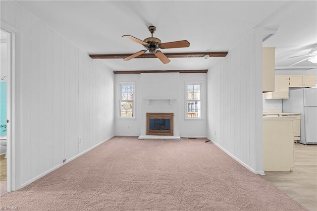 unfurnished living room with baseboards, beamed ceiling, light colored carpet, a glass covered fireplace, and a ceiling fan