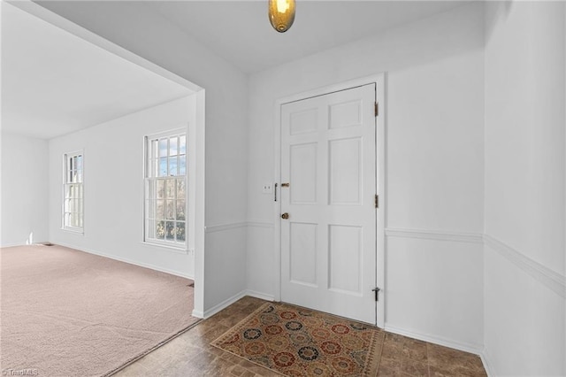 foyer featuring baseboards and carpet