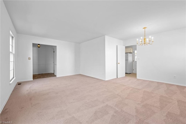 empty room featuring baseboards, a chandelier, and light carpet