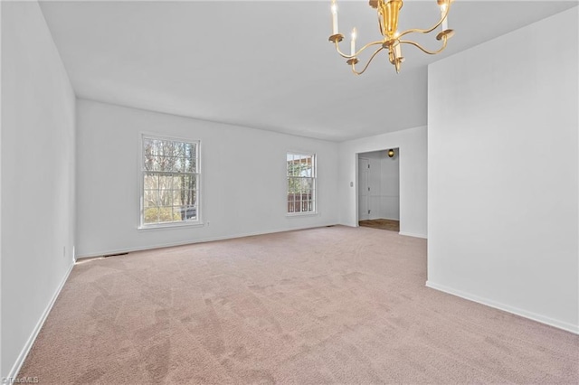 spare room featuring a notable chandelier, carpet flooring, and baseboards