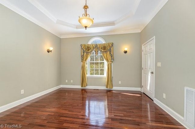 empty room featuring a raised ceiling, visible vents, ornamental molding, wood finished floors, and baseboards