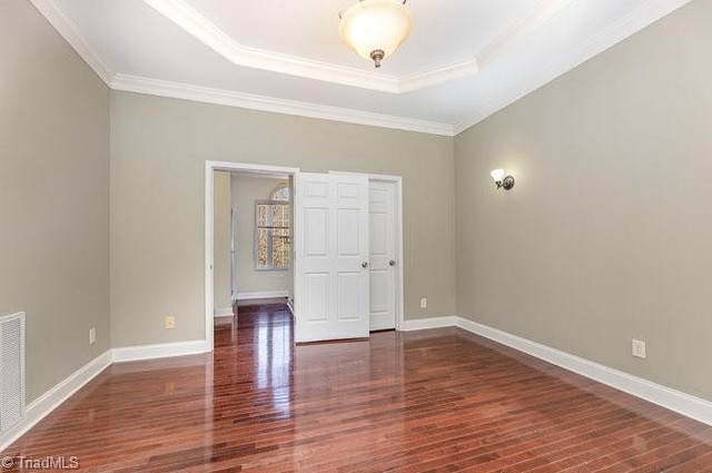 interior space with crown molding, wood finished floors, a raised ceiling, and baseboards