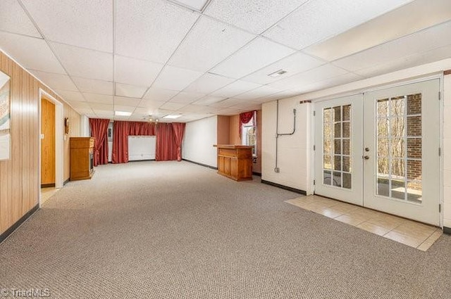 empty room with carpet floors, french doors, wood walls, and a paneled ceiling