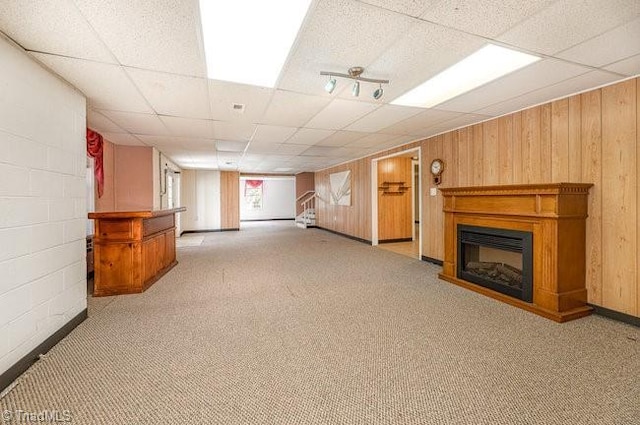 basement featuring carpet floors, a glass covered fireplace, and wood walls