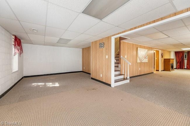 finished basement with carpet flooring, wood walls, stairway, and a drop ceiling