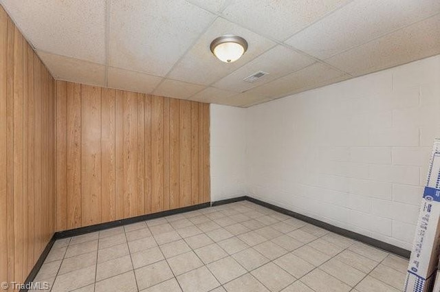 unfurnished room with a drop ceiling, wood walls, and baseboards