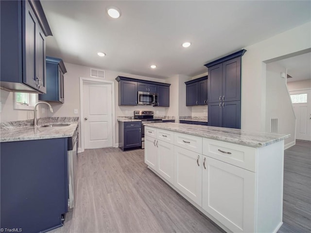 kitchen with white cabinets, light wood-type flooring, appliances with stainless steel finishes, sink, and light stone counters