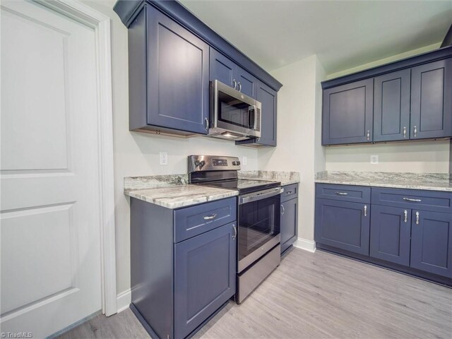 kitchen with appliances with stainless steel finishes, light hardwood / wood-style flooring, and light stone countertops