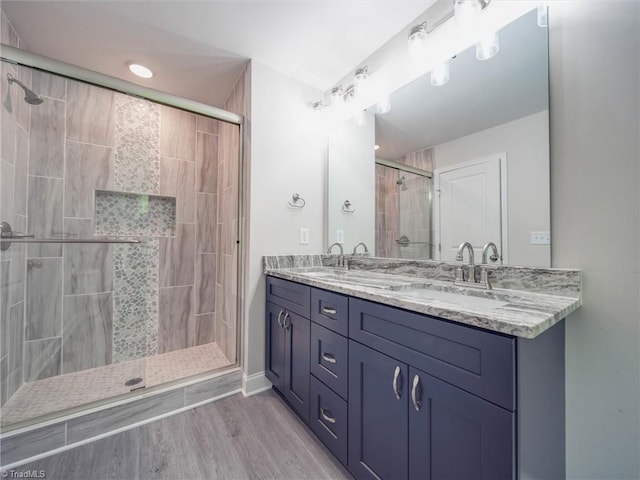 bathroom featuring a shower with door, oversized vanity, hardwood / wood-style flooring, and double sink