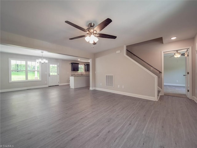 unfurnished living room with ceiling fan with notable chandelier and dark wood-type flooring