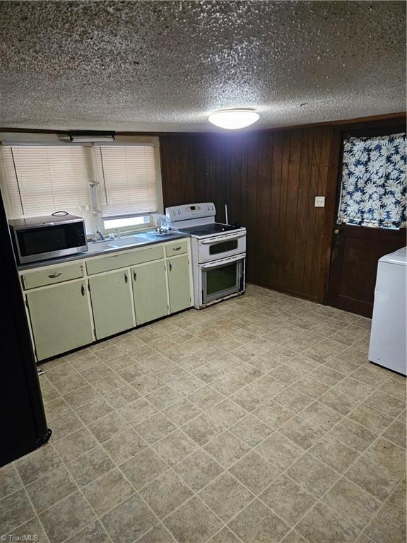 kitchen featuring wooden walls, range with two ovens, washer / clothes dryer, freestanding refrigerator, and stainless steel microwave