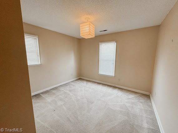 empty room featuring light carpet, a textured ceiling, and baseboards