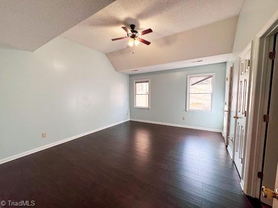 unfurnished room with vaulted ceiling, dark wood-style flooring, a ceiling fan, and baseboards