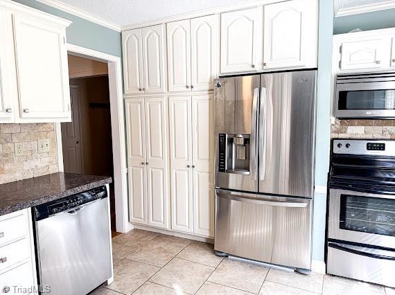 kitchen featuring decorative backsplash, appliances with stainless steel finishes, ornamental molding, white cabinets, and dark stone counters