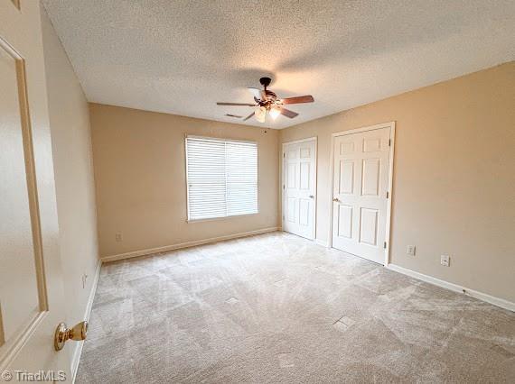 unfurnished bedroom featuring multiple closets, light carpet, ceiling fan, a textured ceiling, and baseboards