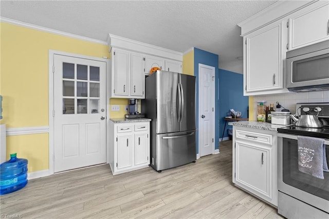 kitchen featuring light wood-type flooring, ornamental molding, tasteful backsplash, appliances with stainless steel finishes, and white cabinets