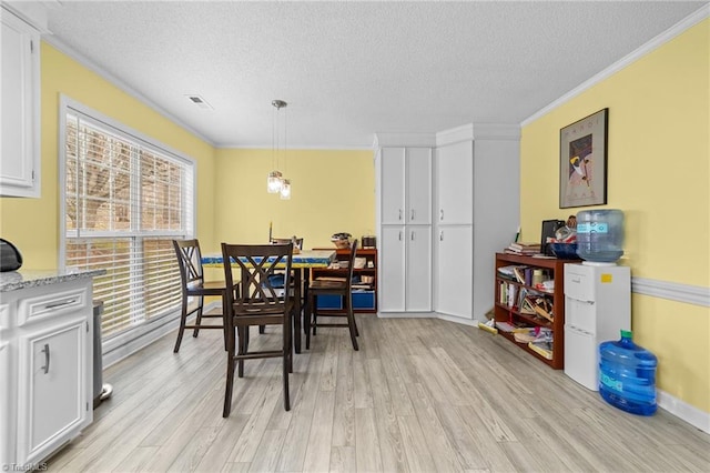 dining space featuring light wood finished floors, visible vents, a textured ceiling, and crown molding