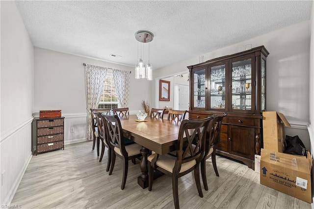 dining area with light wood-style flooring, visible vents, wainscoting, and a textured ceiling