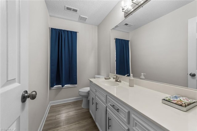 bathroom with visible vents, toilet, a textured ceiling, wood finished floors, and vanity