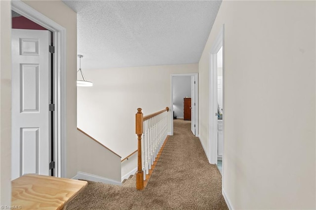 hall with baseboards, an upstairs landing, carpet, and a textured ceiling