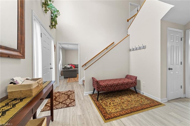 foyer entrance featuring a high ceiling, stairway, light wood-style flooring, and baseboards