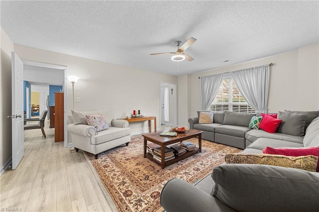 living area featuring a textured ceiling, baseboards, light wood finished floors, and ceiling fan