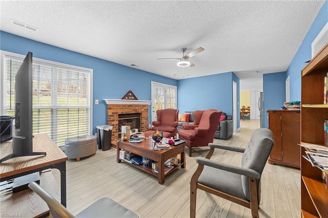 living room with a wealth of natural light, visible vents, a brick fireplace, and light wood-type flooring