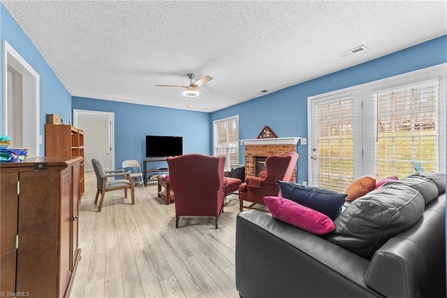 living room with visible vents, a fireplace, ceiling fan, light wood-style floors, and a textured ceiling