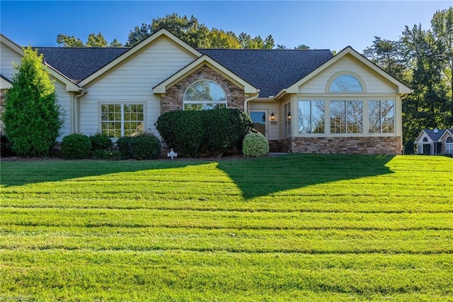 ranch-style house with stone siding, roof with shingles, and a front yard