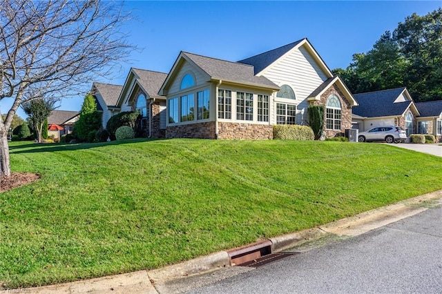 view of front of house featuring an attached garage, stone siding, a front yard, and driveway