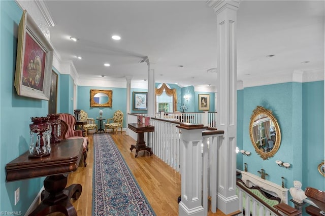 corridor featuring light wood-type flooring, crown molding, and ornate columns